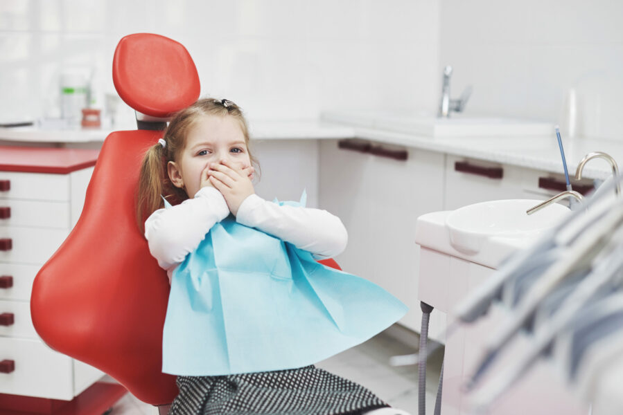young girl sitting in dentist chair and covering her mouth