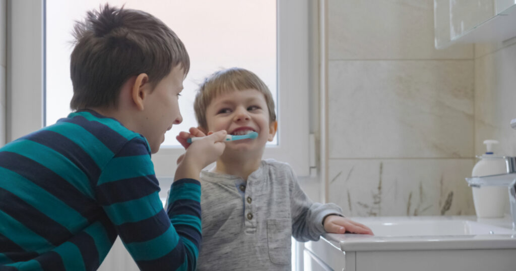 A boy helping his younger brother brush his teeth in a modern bathroom.