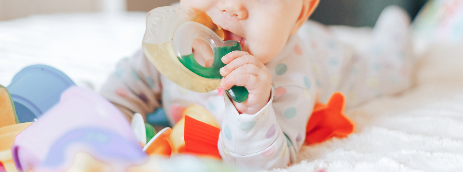Infant lying on bed and chewing on teething toy.