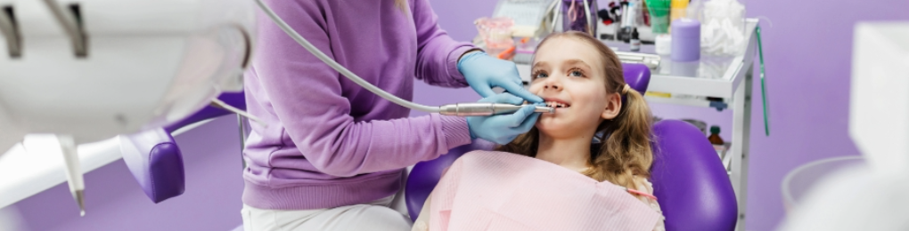 Young girl getting teeth cleaned by a dentist in a lavender operation room.