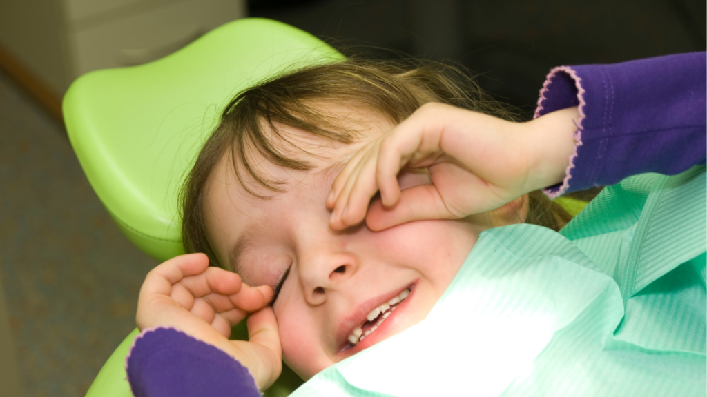 Child in dentist’s chair rubbing eyes.