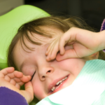 Child in dentist’s chair rubbing eyes.
